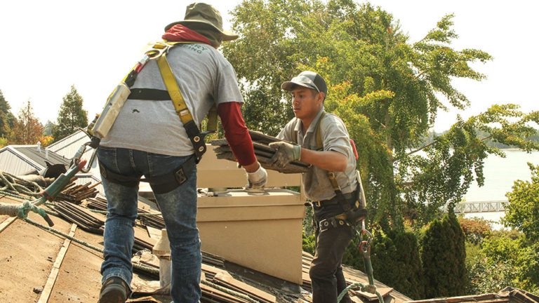 A Cherry Roofing crew member handing shingles to another crew member on the roof of a home.